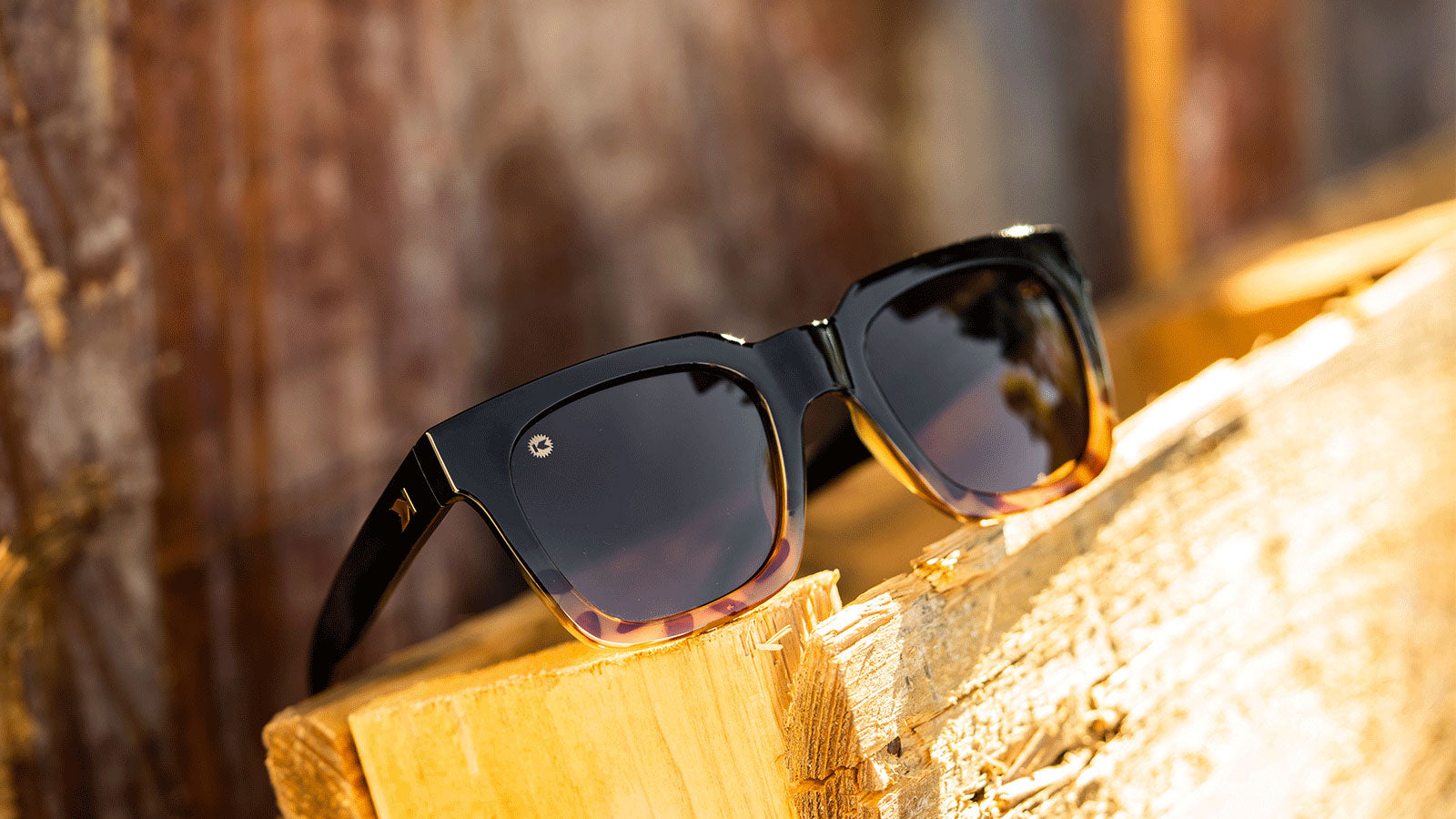 Sunglasses with a glossy black and blonde tortoise shell frame with polarized amber lenses, flyover